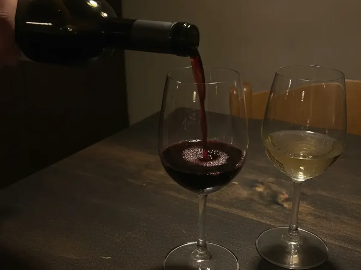 Eine Hand schenkt Rotwein ins Glas, warmes Licht im Gastraum von Punto DiVino
